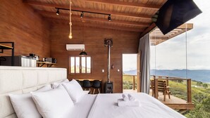 Een slaapkamer met een bed, een bureau met koffieapparaat, een openhaard en een balkon met uitzicht op het landschap.