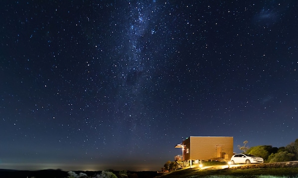 A modern house with a car parked in front, under a starry night sky.