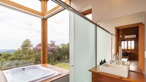 Een moderne badkamer met een groot raam, een jacuzzi en een houten wastafelmeubel.