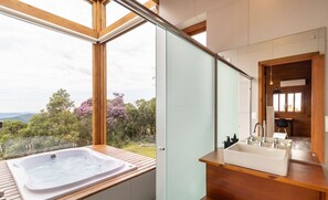 Une salle de bain moderne dotée d’une grande fenêtre, d’une terrasse en bois et d’un jacuzzi.