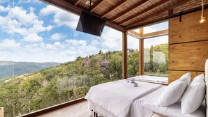 Een slaapkamer met een groot raam, een bed en uitzicht op een bergachtig landschap.