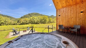 Ein Whirlpool auf einer Holzterrasse mit Blick auf eine grüne Landschaft und Hügel.