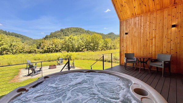 A hot tub on a wooden deck with a view of a green landscape and hills.