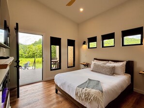 A bedroom with a large bed, a sliding glass door leading to an outdoor area, and multiple windows.
