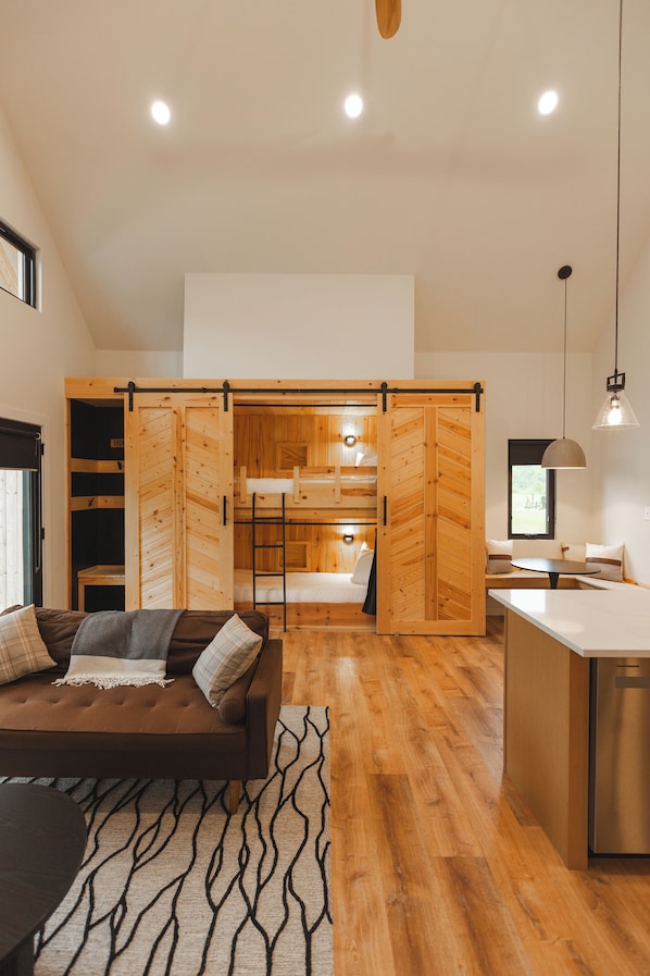 A modern interior with a wooden floor, a sofa with cushions, a dining area, and a kitchen with wooden cabinets.