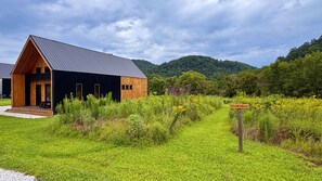 A cabin with a dark exterior and a sloped roof, surrounded by a grassy area and a sign indicating a river trail.