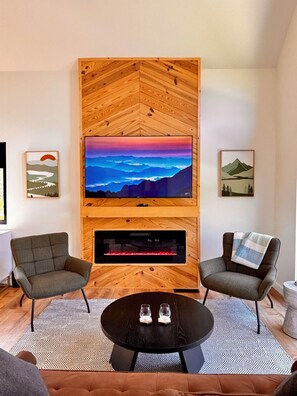 A modern living room with a fireplace, two armchairs, a coffee table, and a TV mounted on a wooden wall. - Knob Hill - River BEACH, Hot Tub, 360 VIEWS, Romantic (Stanton)