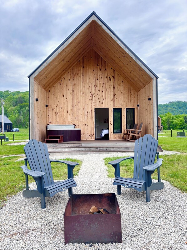Une cabane en bois dotée d’une véranda, de deux fauteuils Adirondack, d’un foyer et offrant une vue sur un paysage verdoyant.