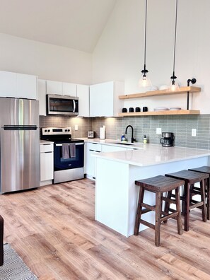 Une cuisine moderne dotée d’appareils électroménagers en acier inoxydable, d’un îlot central, de tabourets en bois et d’un pare-feu en carreaux.