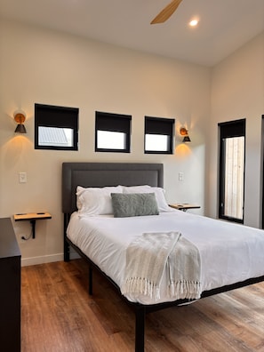 Un dormitorio con cama, mesitas de noche, lámpara de pared y ventana con vistas.