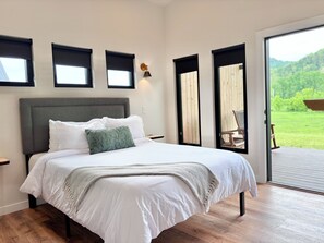 Un dormitorio con una cama grande, cabecera, mesita de noche, lámpara y vistas al exterior a través de una puerta.
