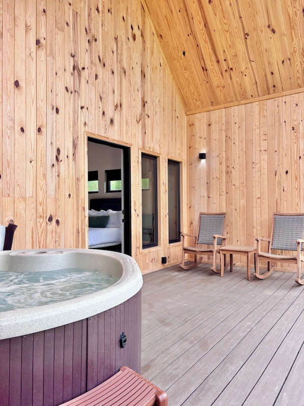 Una cabaña de madera con un jacuzzi, dos mecedoras y una cama.
