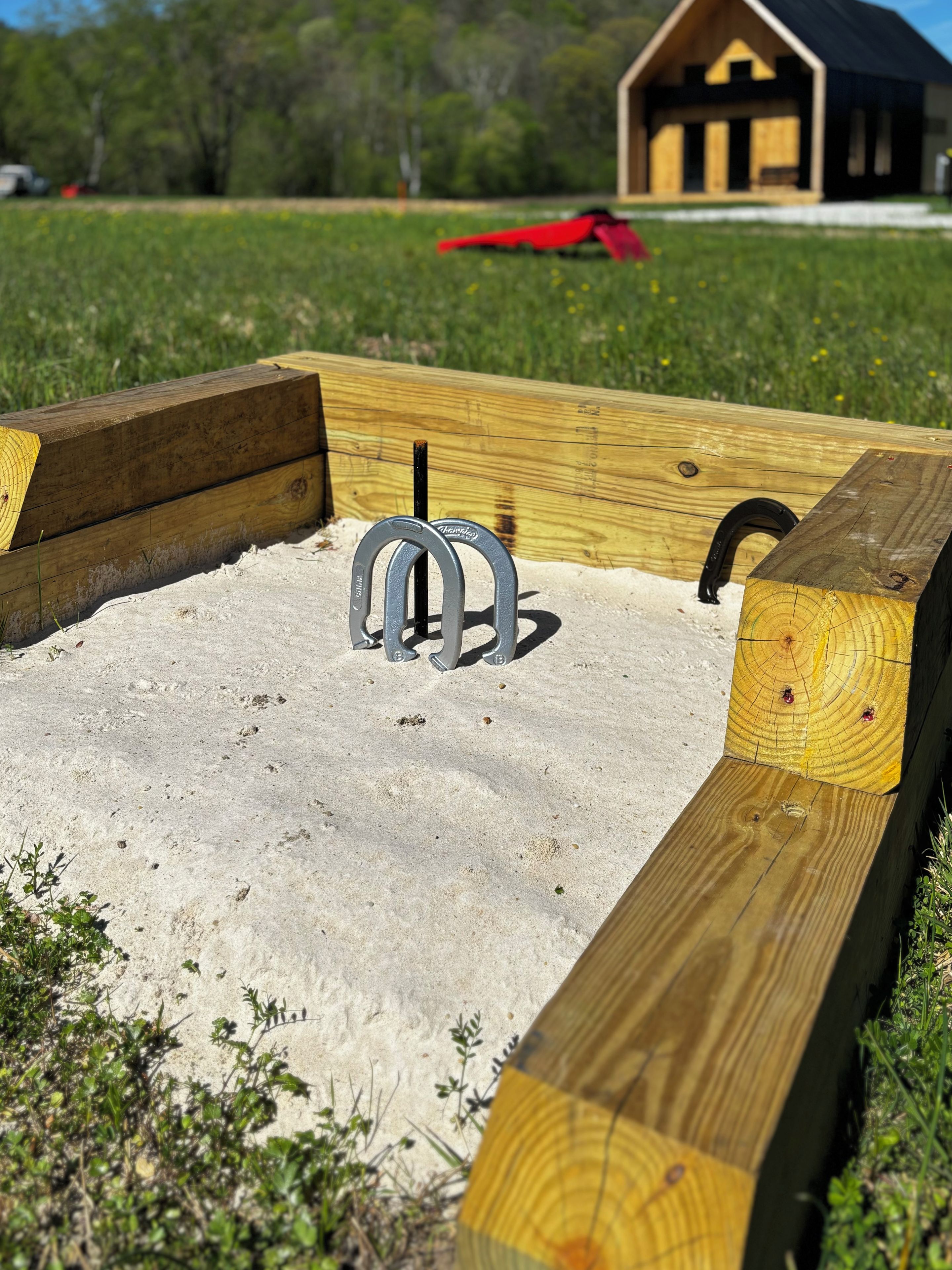 A sandbox with a metal play structure, wooden benches, and a building in the background.