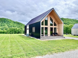 A modern building with a large entrance and a sloped roof, surrounded by a grassy field and forested hills.