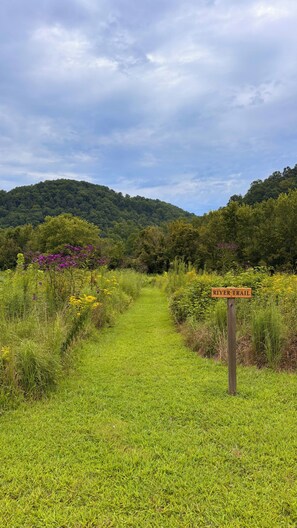 A grassy path leading to a hill with a sign reading 'RIVER TRAIL'.