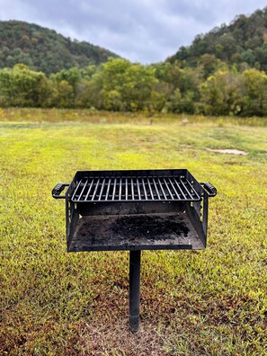 Ein Grill im Gras mit hügeliger Landschaft im Hintergrund.