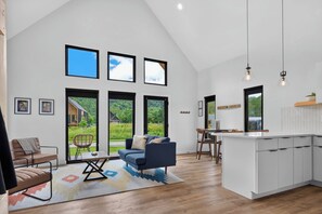 Amplia sala de estar con un ventanal grande, un sofá, una mesa de comedor y una zona de cocina con armarios y encimera.