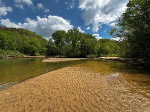 A riverbank with clear water, surrounded by lush greenery and trees. - Perfect Perch - RARE River with BEACH, Sunsets and Stars, Hot Tub, Mountain View (Stanton)