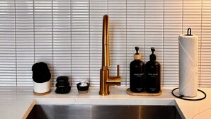 A modern kitchen with a stainless steel sink, a gold faucet, and a wooden countertop. There are two white spherical objects on a shelf above the sink. - Perfect Perch - RARE River with BEACH, Sunsets and Stars, Hot Tub, Mountain View (Stanton)