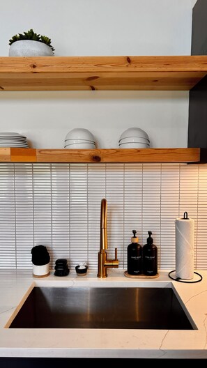 A modern kitchen with a stainless steel sink, a gold faucet, and a wooden countertop. There are two white spherical objects on a shelf above the sink.