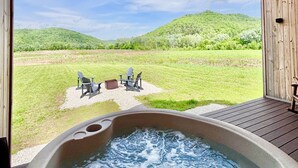 A hot tub with a view of a grassy field and hills. - Perfect Perch - RARE River with BEACH, Sunsets and Stars, Hot Tub, Mountain View (Stanton)