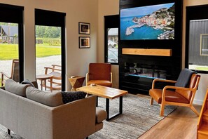 A living room with a sofa, chairs, a coffee table, and a fireplace. There is a television mounted on the wall displaying a scenic view.