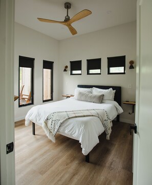 Une chambre à coucher avec un lit, un ventilateur de plafond et trois fenêtres équipées de stores.