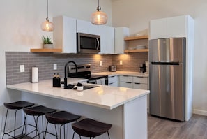A modern kitchen with a central island, bar stools, a stainless steel refrigerator, a microwave, and pendant lighting.