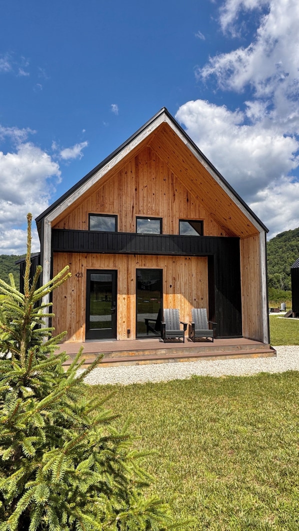 Una casa moderna de madera con techo inclinado, ventanas grandes y un porche cubierto con mobiliario exterior.