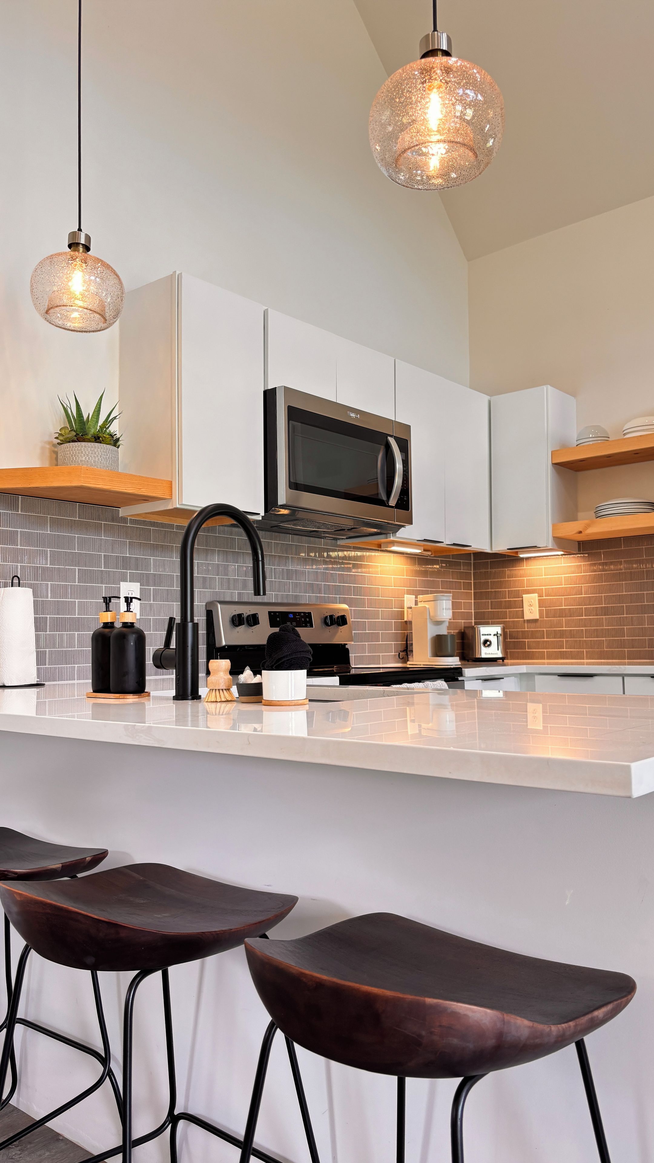 A modern kitchen with a central island, bar stools, a microwave, and pendant lighting.
