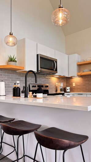 A modern kitchen with a central island, bar stools, a microwave, and pendant lighting. - Wildflower Walk - Sunset Views, River with BEACH, Hot Tub, Walking Trails (Stanton)
