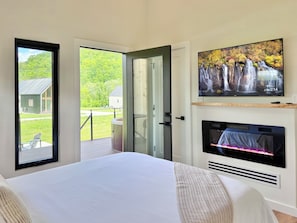 A bedroom with a bed, a TV, a fireplace, and a view of a green landscape. - Trail Tamer - Gorgeous 360 Views, RIVER with sandy BEACH, Hot Tub, RRGorge (Stanton)