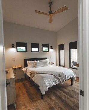 A bedroom with a bed, wooden floor, ceiling fan, bedside tables, and wall-mounted lights.