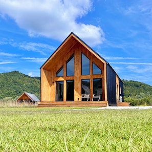 A wooden cabin with a large porch, large windows, and a view of a forested hill. - Trail Tamer - Gorgeous 360 Views, RIVER with sandy BEACH, Hot Tub, RRGorge (Stanton)