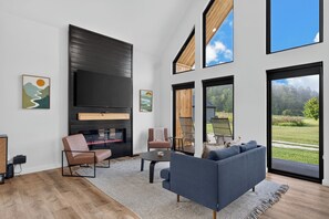 Ein modernes Wohnzimmer mit Kamin, Sitzgelegenheiten und großen Fenstern mit Blick ins Freie.