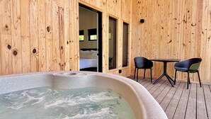 A wooden cabin interior with a hot tub, a dining table with chairs, and a bedroom visible through an open door. - Trail Tamer - Gorgeous 360 Views, RIVER with sandy BEACH, Hot Tub, RRGorge (Stanton)
