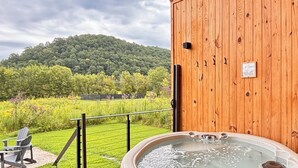Una terraza de madera con un jacuzzi, vista a un paisaje verde y cielo nublado.