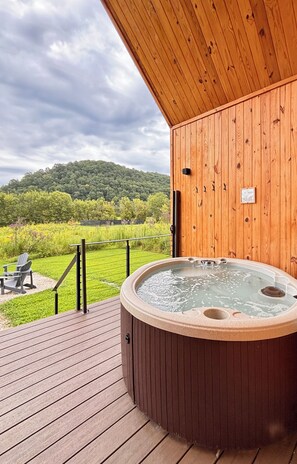 Una terraza de madera con un jacuzzi, vista a un paisaje verde y cielo nublado.