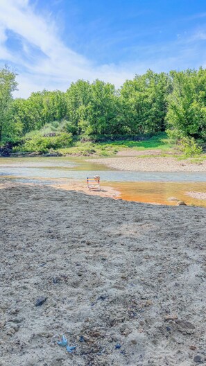 A riverbank with a beach chair, trees, and a clear sky.