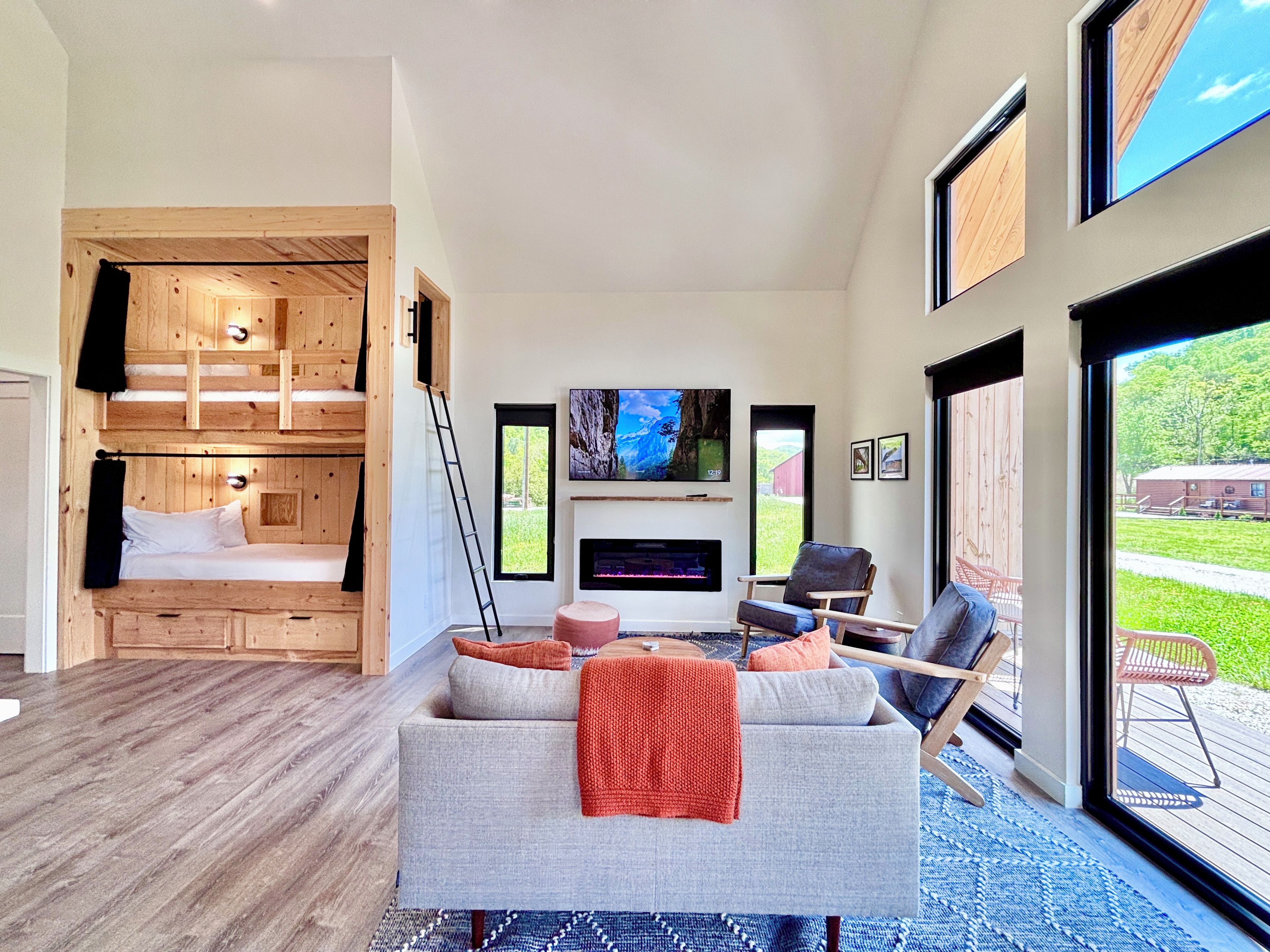 A modern living room with a sofa, chairs, a fireplace, a TV, and a wooden bunk bed.