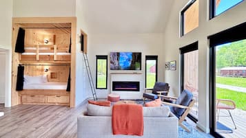A modern living room with a sofa, chairs, a fireplace, a TV, and a wooden bunk bed.