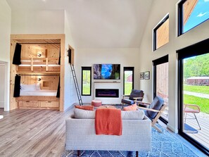 A modern living room with a sofa, chairs, a fireplace, a TV, and a wooden bunk bed. - Moonrise Meadow | RARE River BEACH, Hot Tub, RRG (Stanton)