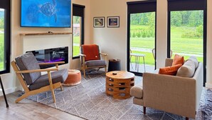 Una sala de estar moderna con televisor de pantalla plana, asientos cómodos, chimenea y ventanas amplias con vistas al exterior.