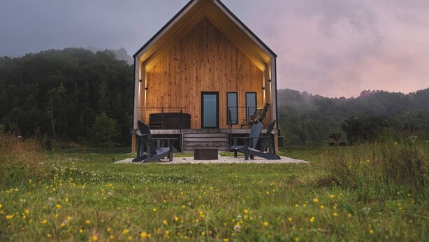Une cabane en bois avec une véranda, deux fenêtres et une cheminée.