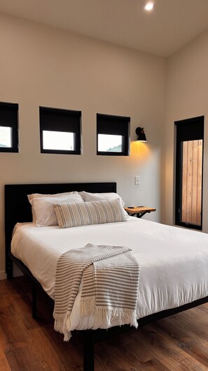A bedroom with a bed, a bedside table, and a lamp. - Three Suns Cabins: All 8 Cabins, Sleeps 29, Private Beach, RRG (Stanton)