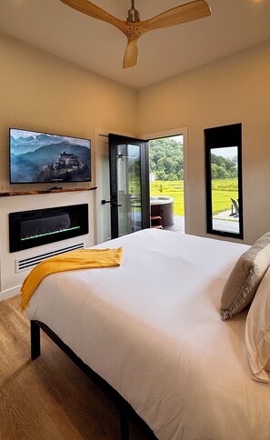 A bedroom with a bed, a television mounted on the wall, and a view of a mountainous landscape through a window.