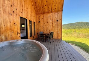 Uma cabana de madeira com hidromassagem, área de refeições e vista para uma paisagem verde.