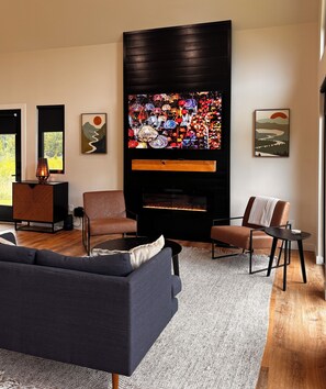 A modern living room with a flat-screen TV, two armchairs, a sofa, and a fireplace. - Three Suns Cabins: All 8 Cabins, Sleeps 29, Private Beach, RRG (Stanton)
