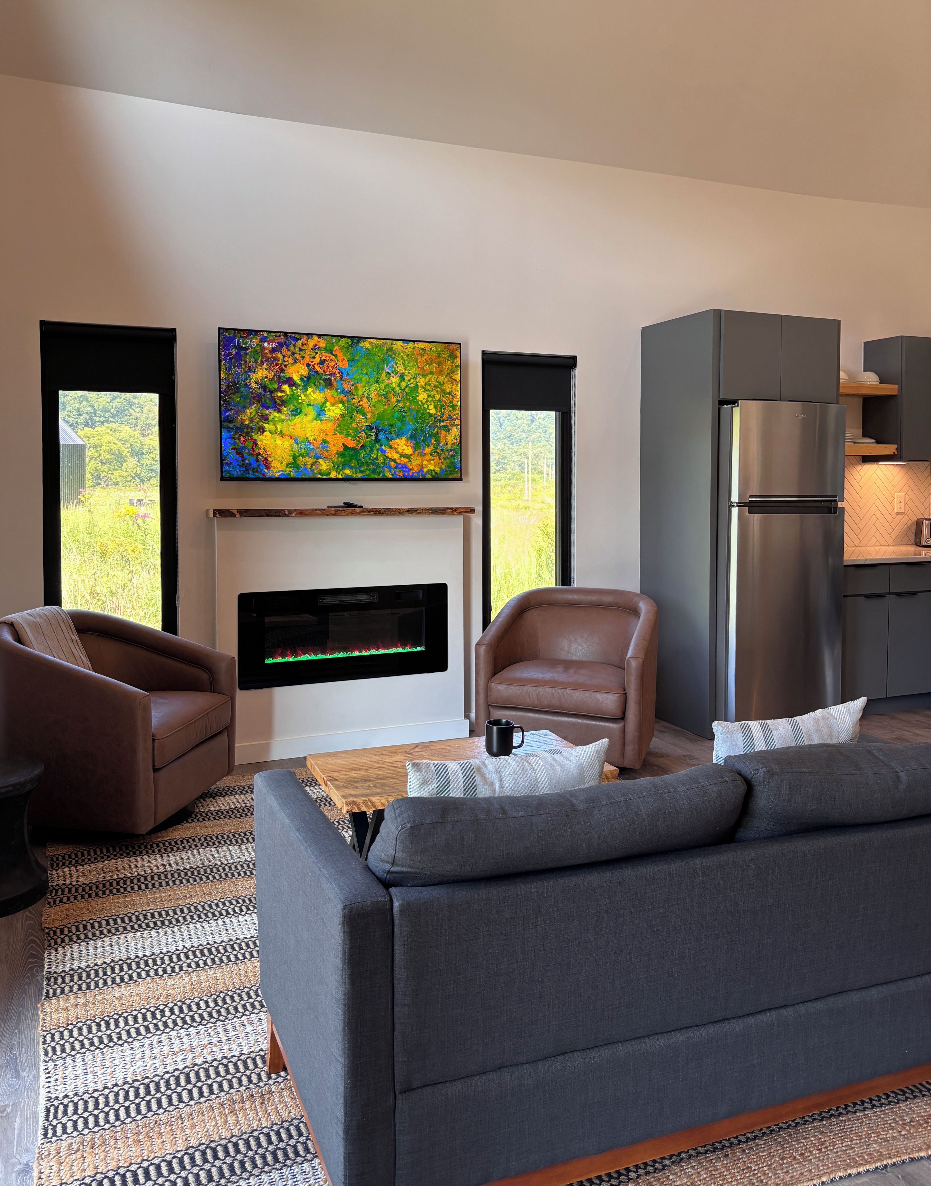 Een moderne woonkamer met een bank, fauteuils, een flatscreen televisie, een open haard en een keukenhoek.