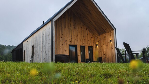 Une grange en bois, dotée d’un toit à pente, de grandes portes et de deux fenêtres à l’avant.
